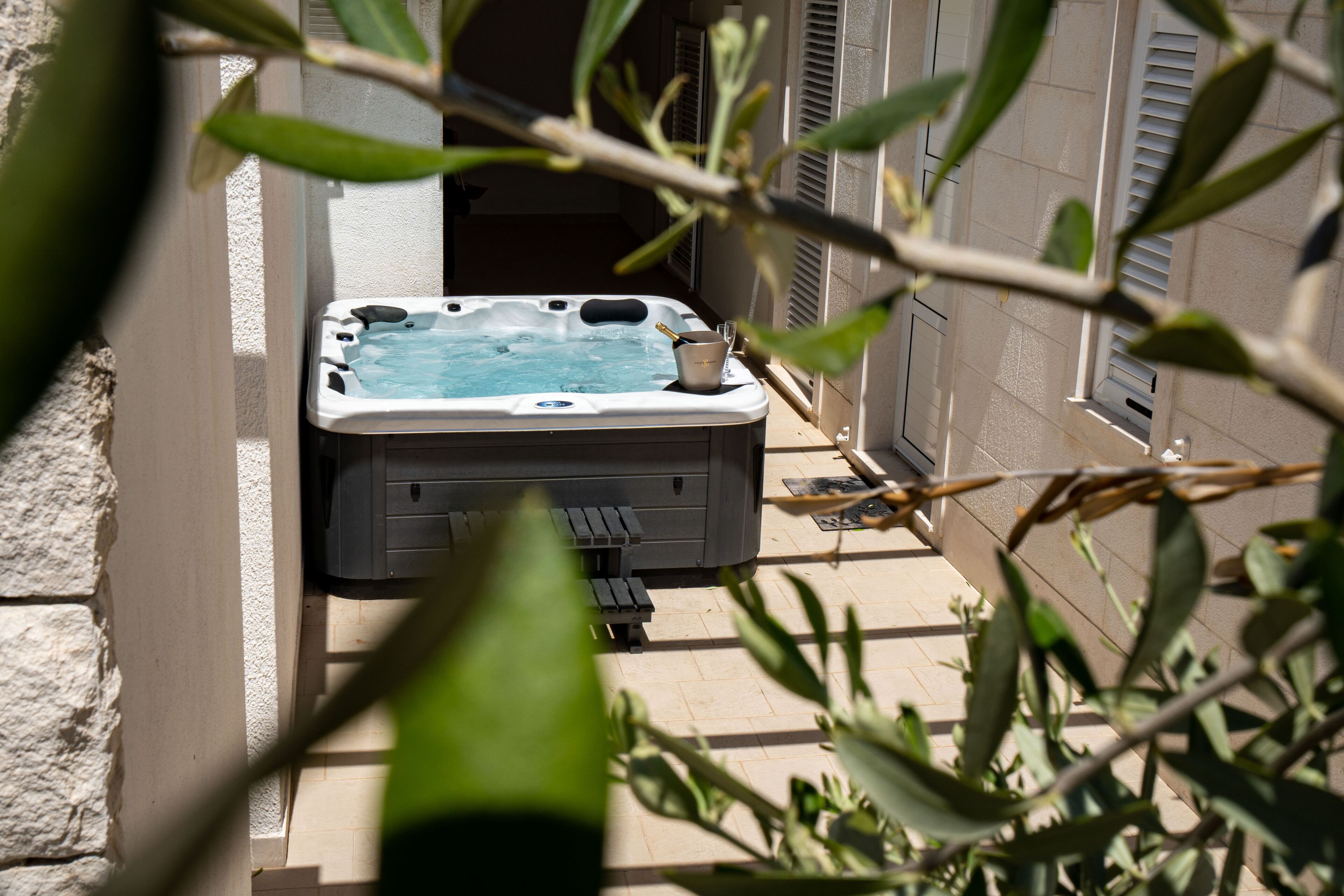 A hot tub in a covered outdoor area with a brick wall and a window with shutters.