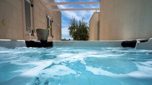 A hot tub with a champagne bottle and glasses, surrounded by beige walls and a tree in the background. - Villa Azzurra (Bol)