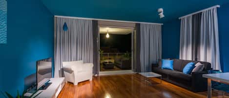 Een moderne woonkamer met een televisie, een witte bank en een donkere bank met blauwe kussens.