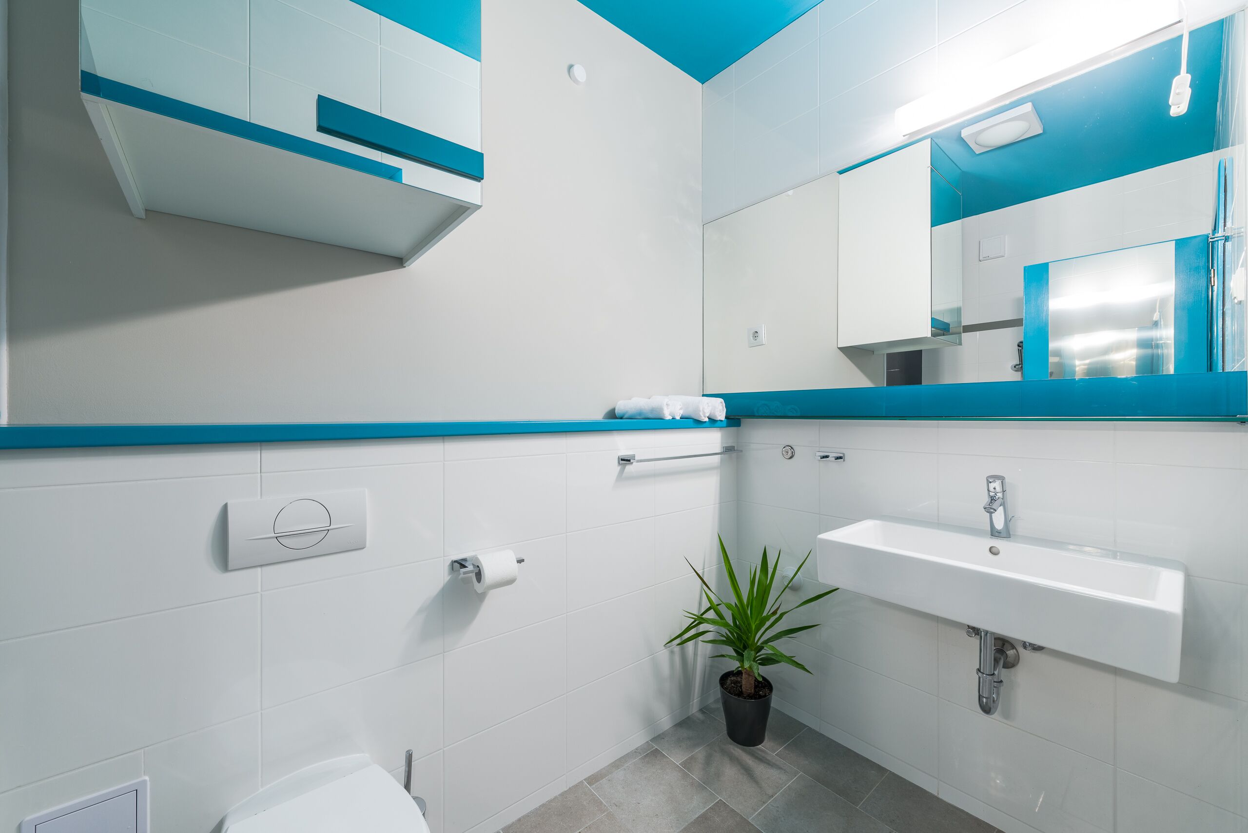 A modern bathroom with a white and blue color scheme, a sink, a toilet, and a mirror.