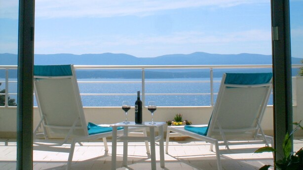 A balcony with two white lounge chairs, a small table, and a bottle of wine. - Villa Azzurra (Bol)