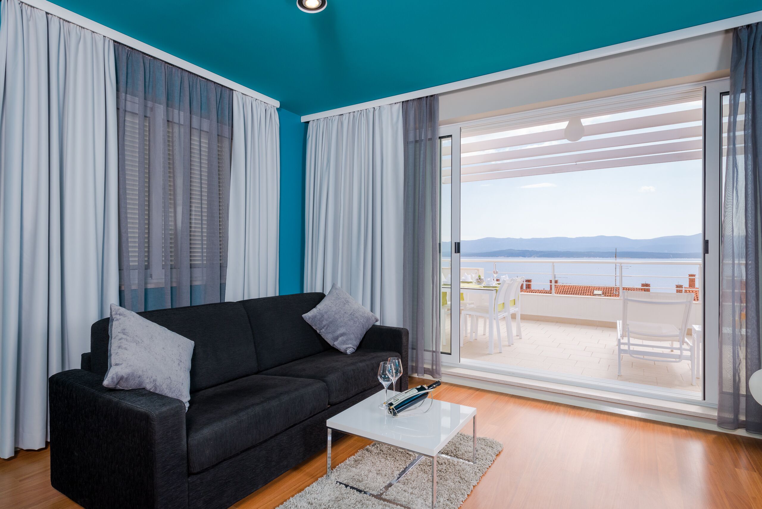 En moderne stue med en sort sofa, et hvidt sofabord og udsigt til en terrasse med udendørs møbler.