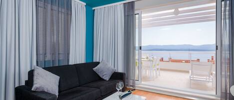 A modern living room with a black sofa, a white coffee table, and a view of a terrace with outdoor furniture.