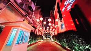 A narrow alleyway with buildings on either side, illuminated by hanging lanterns and a neon sign. - The Cosy River (Bangkok)