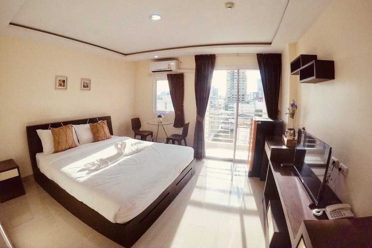 A hotel room with a large bed, a desk with a computer, a TV, and a view of the city through the window.