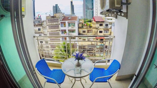 A balcony with two blue chairs and a small table, overlooking a cityscape with various buildings. - The Cosy River (Bangkok)
