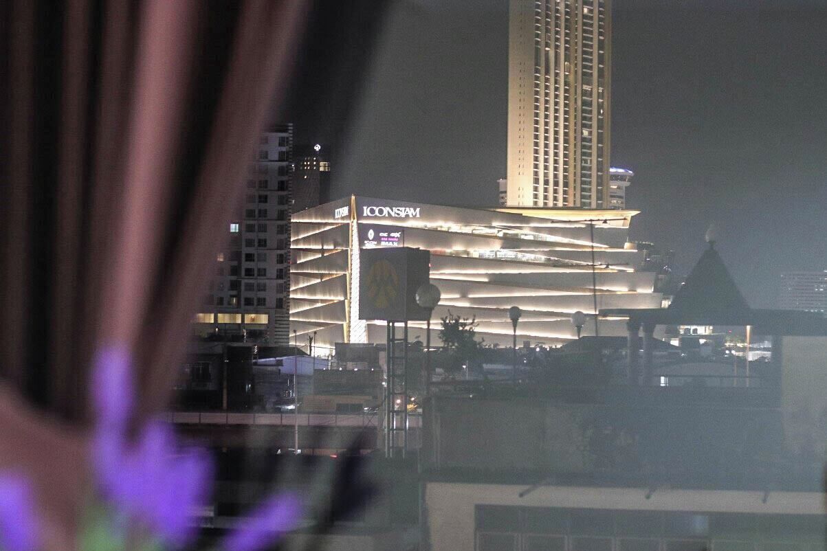 A modern building with the ICONSIAM logo, featuring a unique architectural design with multiple levels and a prominent water tank on the roof.