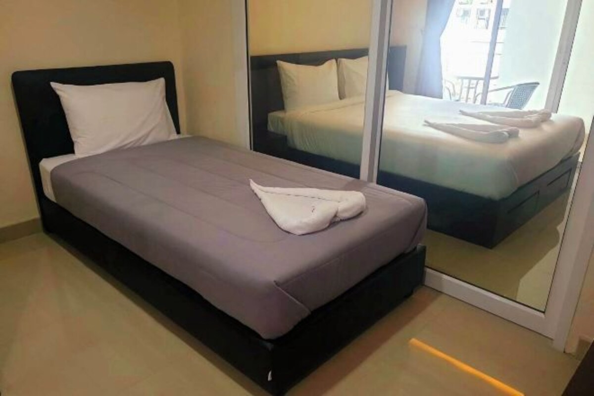 A single bed with a grey mattress and white pillows in a room with a large window.