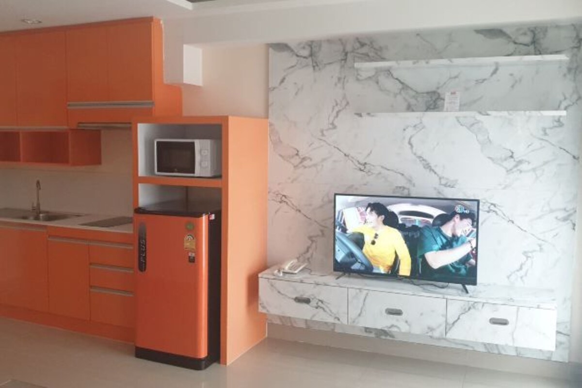 A modern kitchen with orange cabinets, a microwave, and a marble backsplash.
