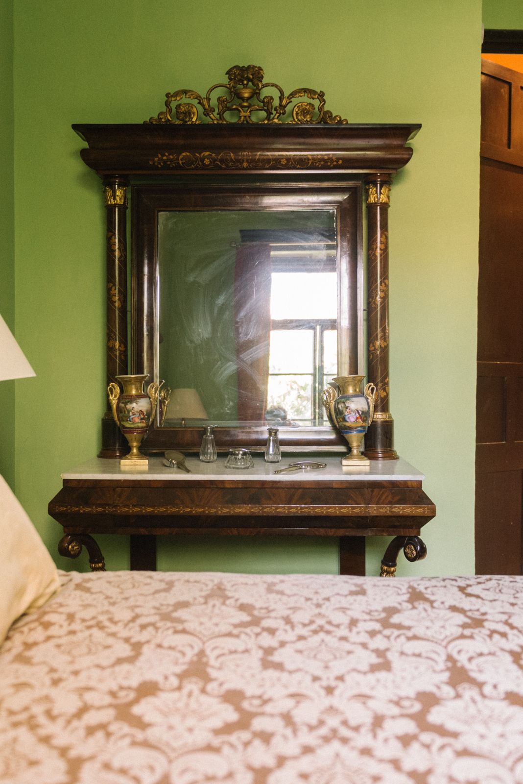 Um quarto com um espelho grande sobre um pente de madeira, uma cama com colcha estampada e uma parede verde.