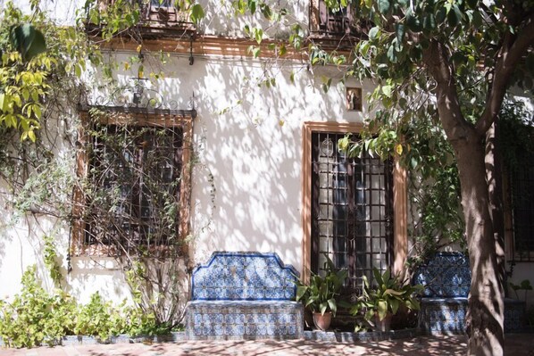 A courtyard with a tiled bench, potted plants, and a tree. - Palacio del Virrey Laserna (Jerez de la Frontera)