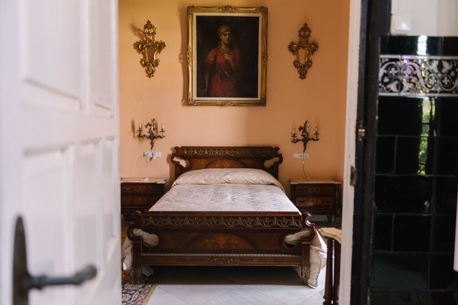 A bedroom with a wooden bed, a painting on the wall, and two wall sconces.