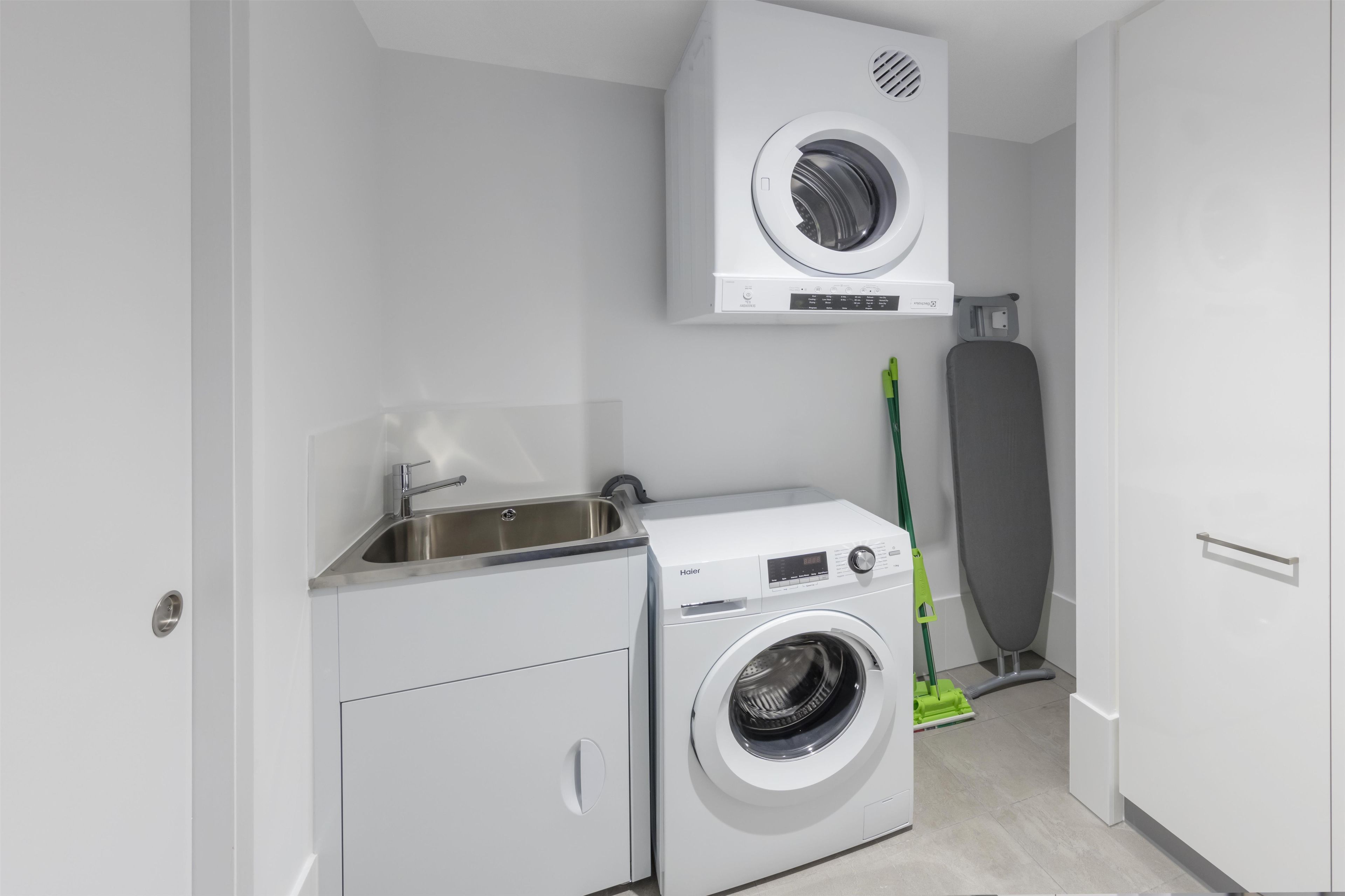 A compact laundry room with a washing machine, a dryer, a sink, and a mop.
