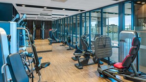 Un gimnasio con diversas máquinas de ejercicio, amplias ventanas y suelo de madera.