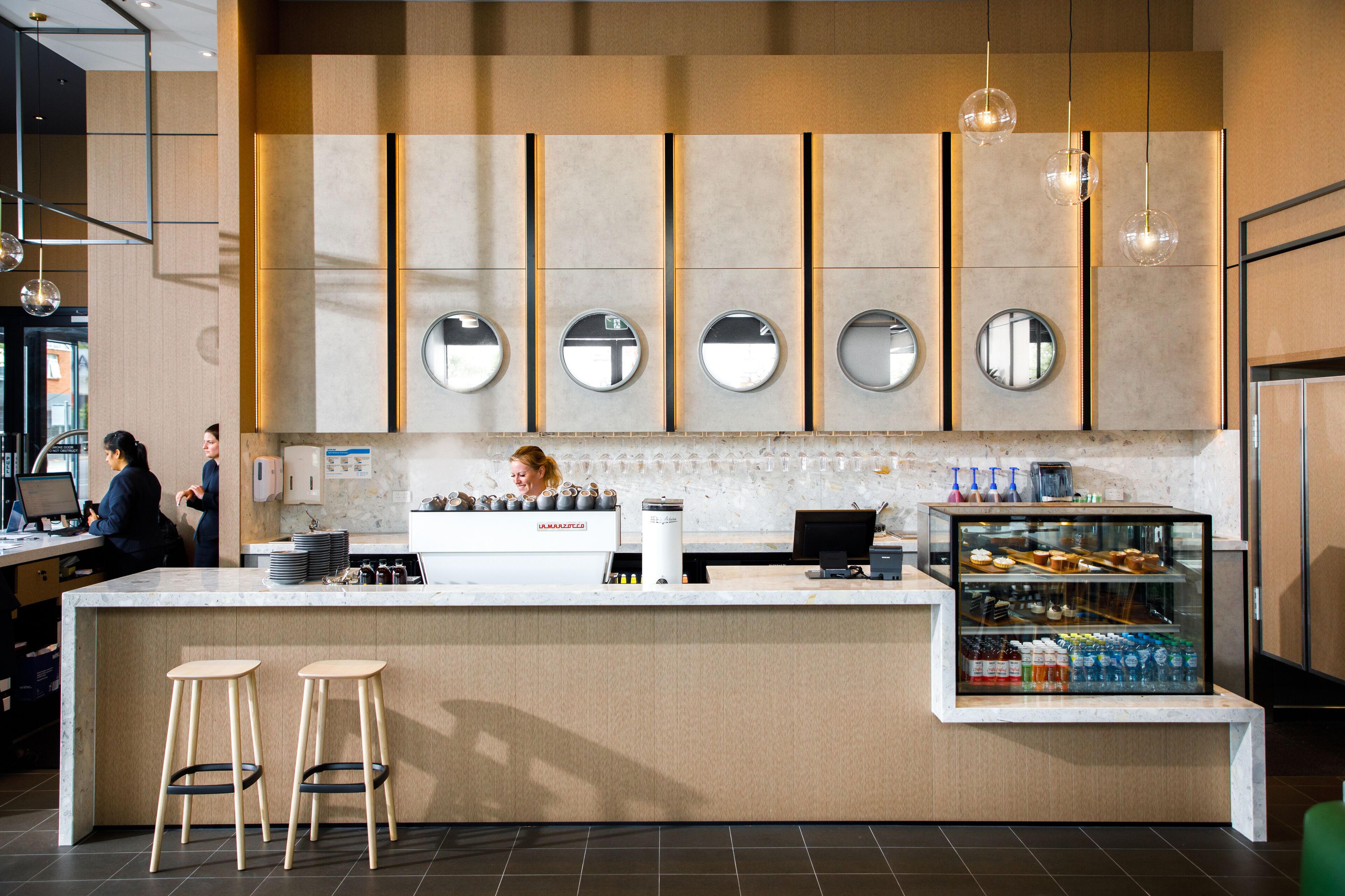 Een modern café met een centraal gelegen toonbank, barstoelen en een vitrine met gebak.