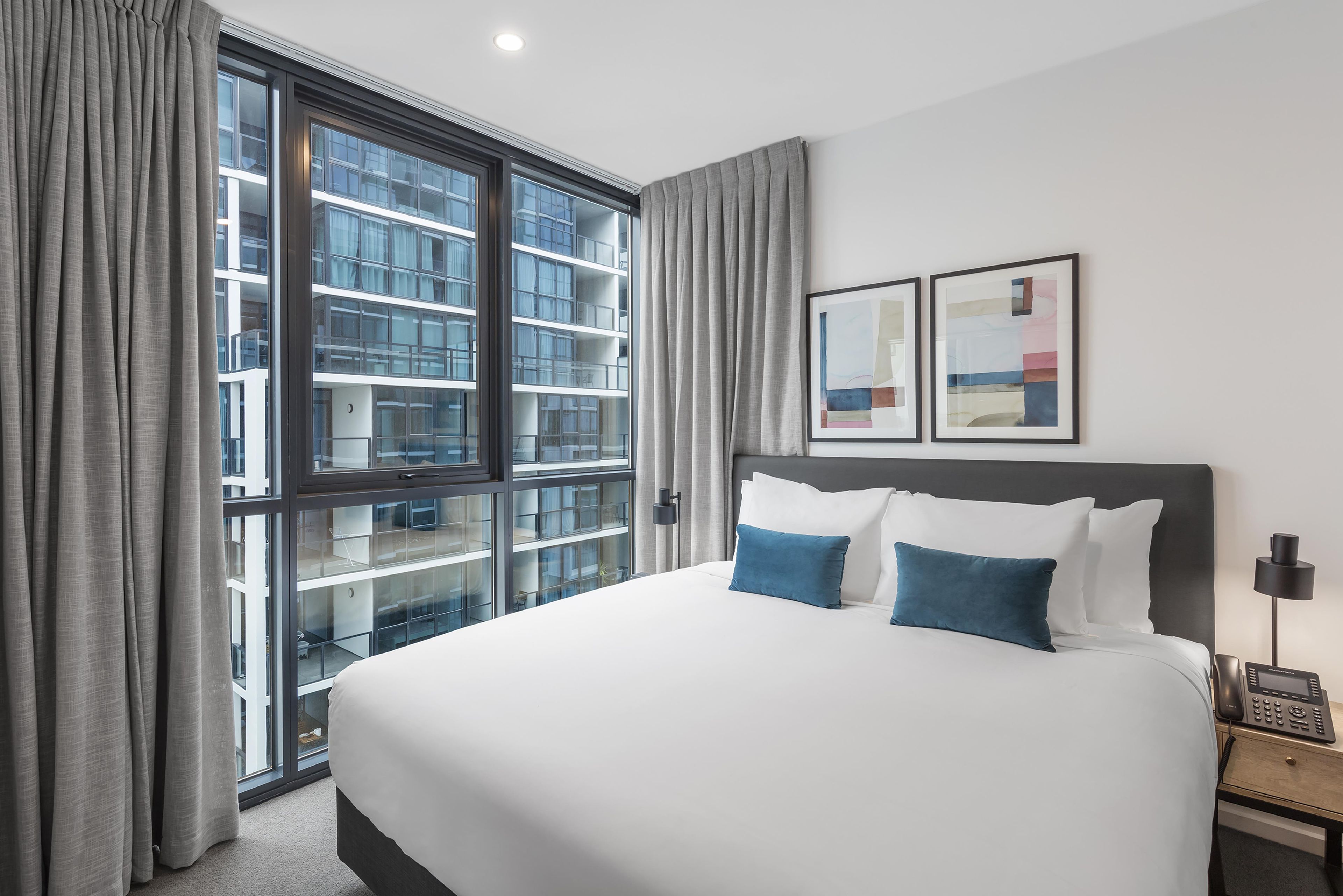 A hotel room with a large bed, a bedside phone, and a window with a view of a building.