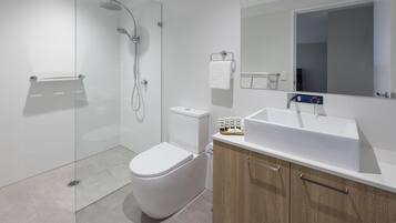 Un bagno moderno con cabina doccia in vetro, un water bianco, un lavabo con uno specchio sopra e mobili in legno.
