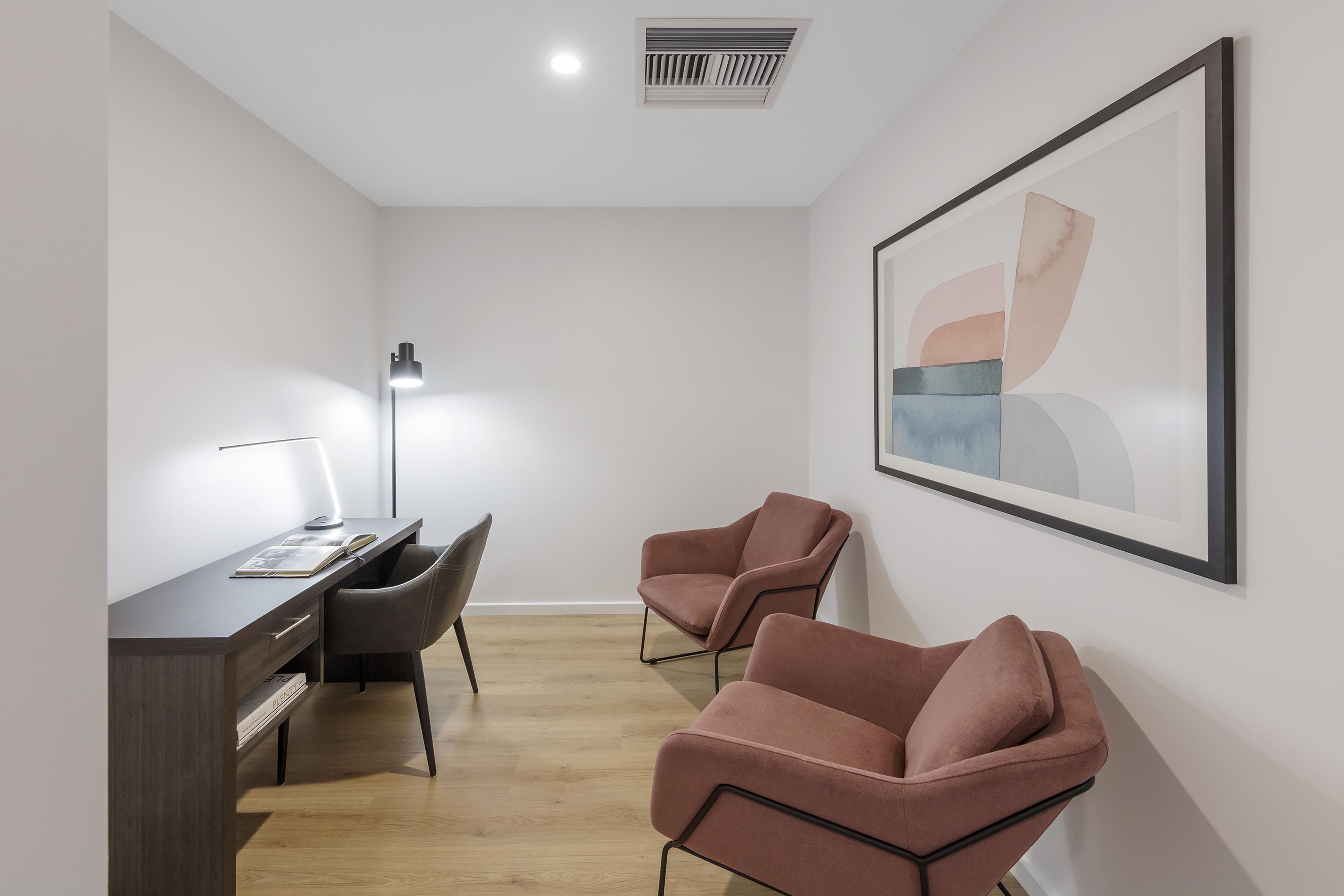 Une chambre moderne équipée d’un bureau, de deux chaises, d’un lampadaire et d’une œuvre d’art abstraite encadrée accrochée au mur.