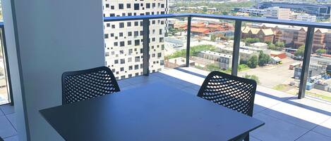 Un balcon avec une table et des chaises, offrant une vue sur le paysage urbain, avec ses bâtiments et ses grues de construction.
