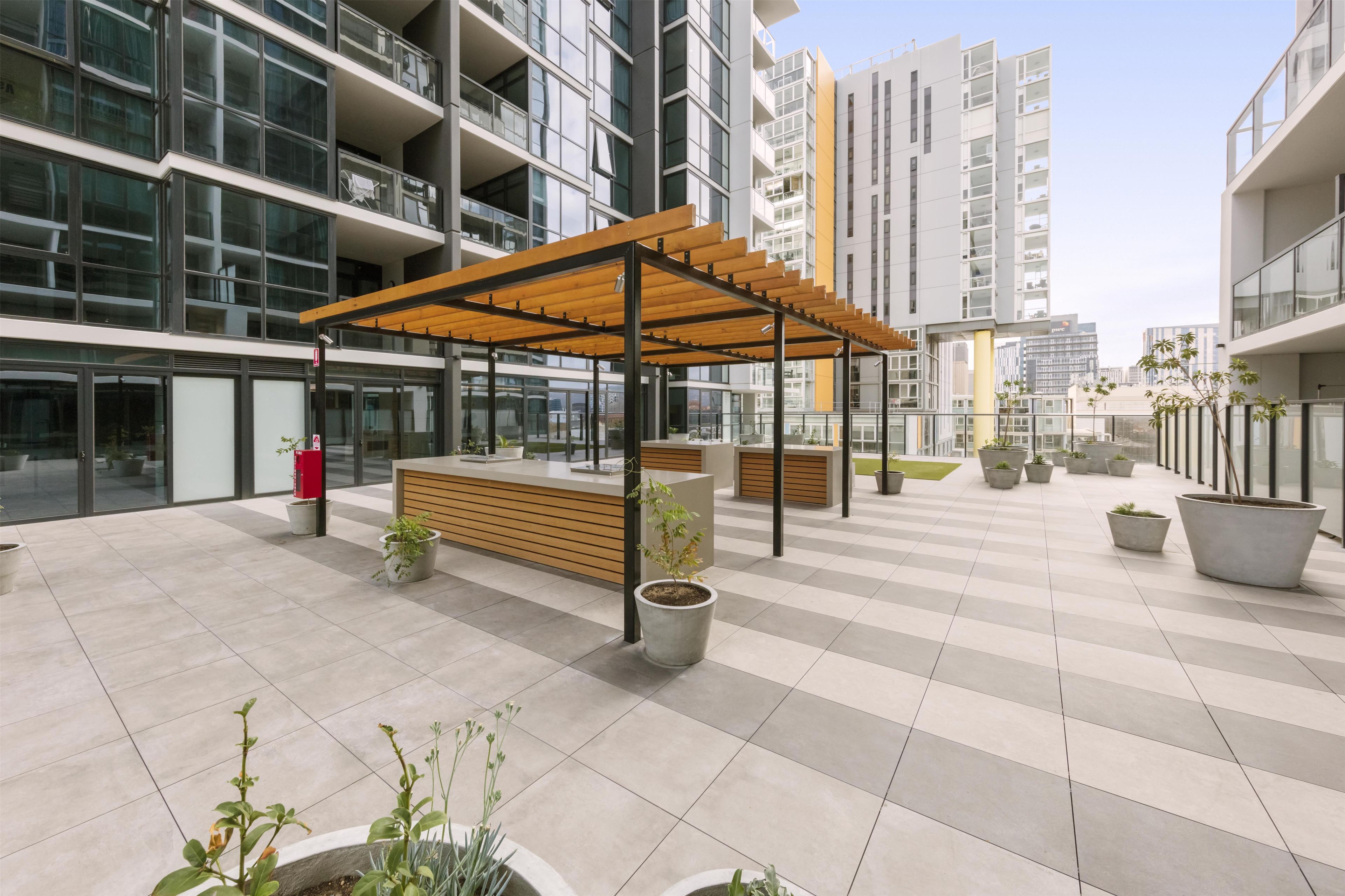 A modern outdoor seating area with a wooden pergola, potted plants, and a reception desk.