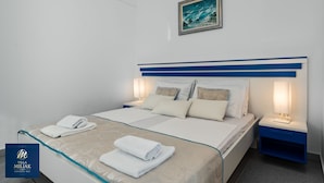 A hotel room with a bed, two bedside tables, a nightstand, a framed picture on the wall, and a logo on the wall. - Villa Miljak (Podstrana)