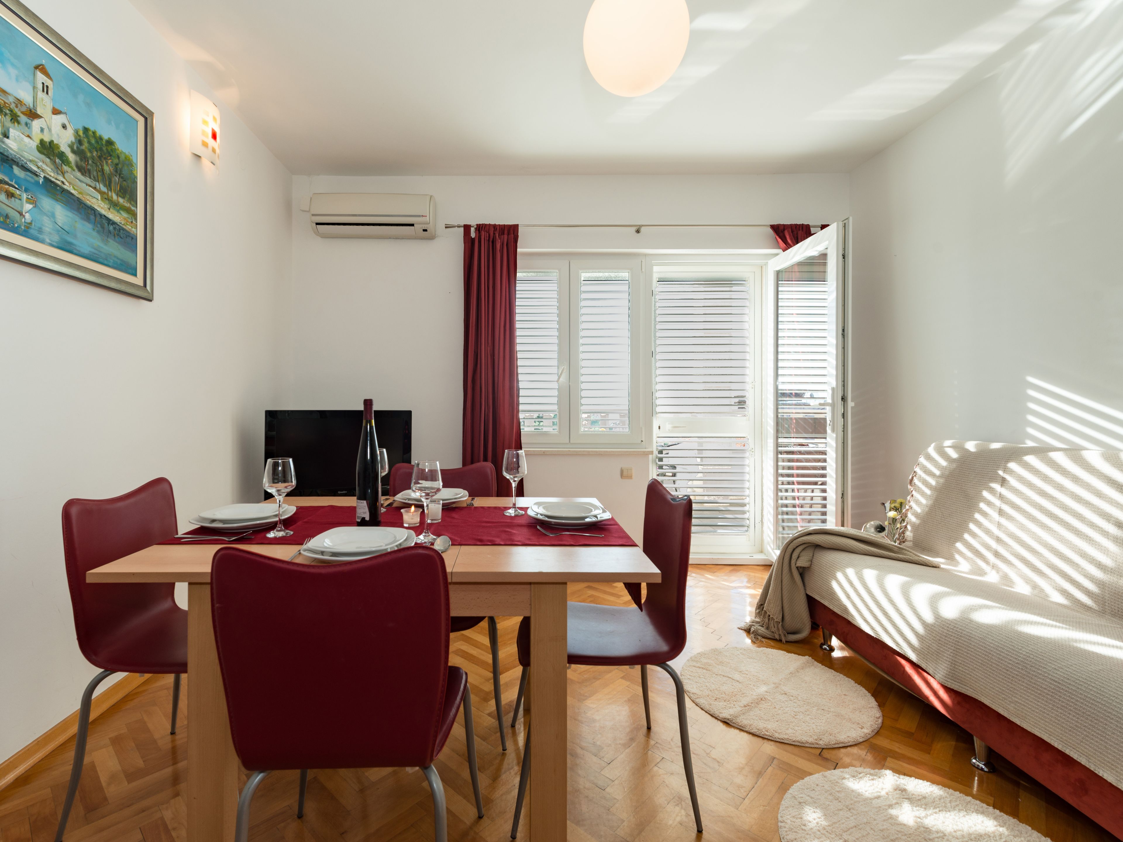 A dining area with a table set for four, red chairs, a TV, and a window with blinds.