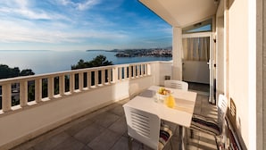 A balcony with a table and chairs, overlooking a body of water and distant land. - Villa Miljak (Podstrana)