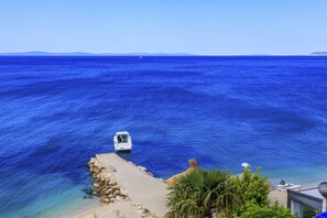 A coastal view with a boat docked at a rocky shore, clear blue sea, and distant landforms. - Ante apartments (Podstrana)