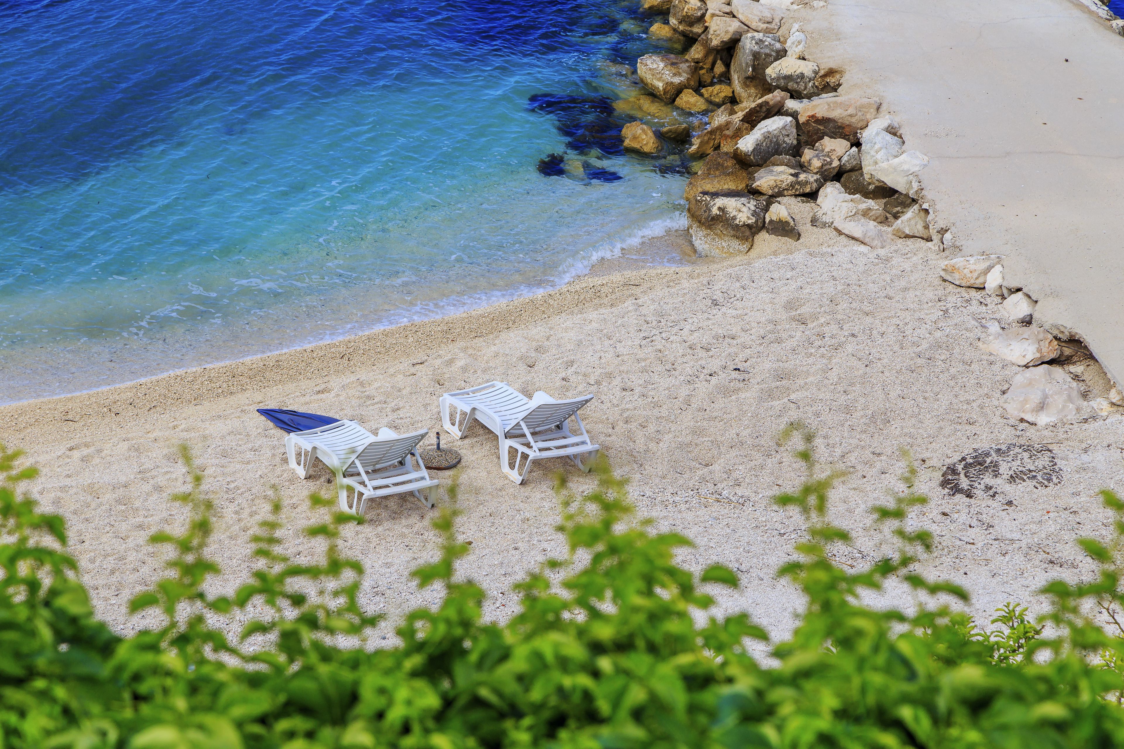 A beach with white lounge chairs and a rocky shoreline.