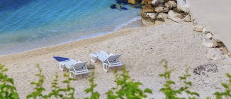 A beach with white lounge chairs and a rocky shoreline.