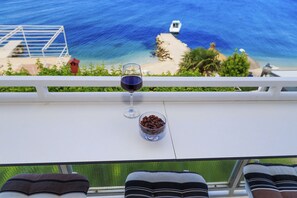 A table with a glass of red wine and a bowl of chocolate chips, overlooking a beach with a boat in the distance. - Ante apartments (Podstrana)