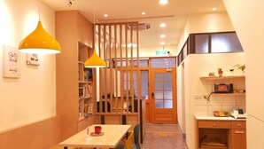 A cozy dining area with wooden furniture, a yellow pendant light, and a kitchen area with a microwave and shelves. - Fu Ao Wo & Hostel (Nangan)