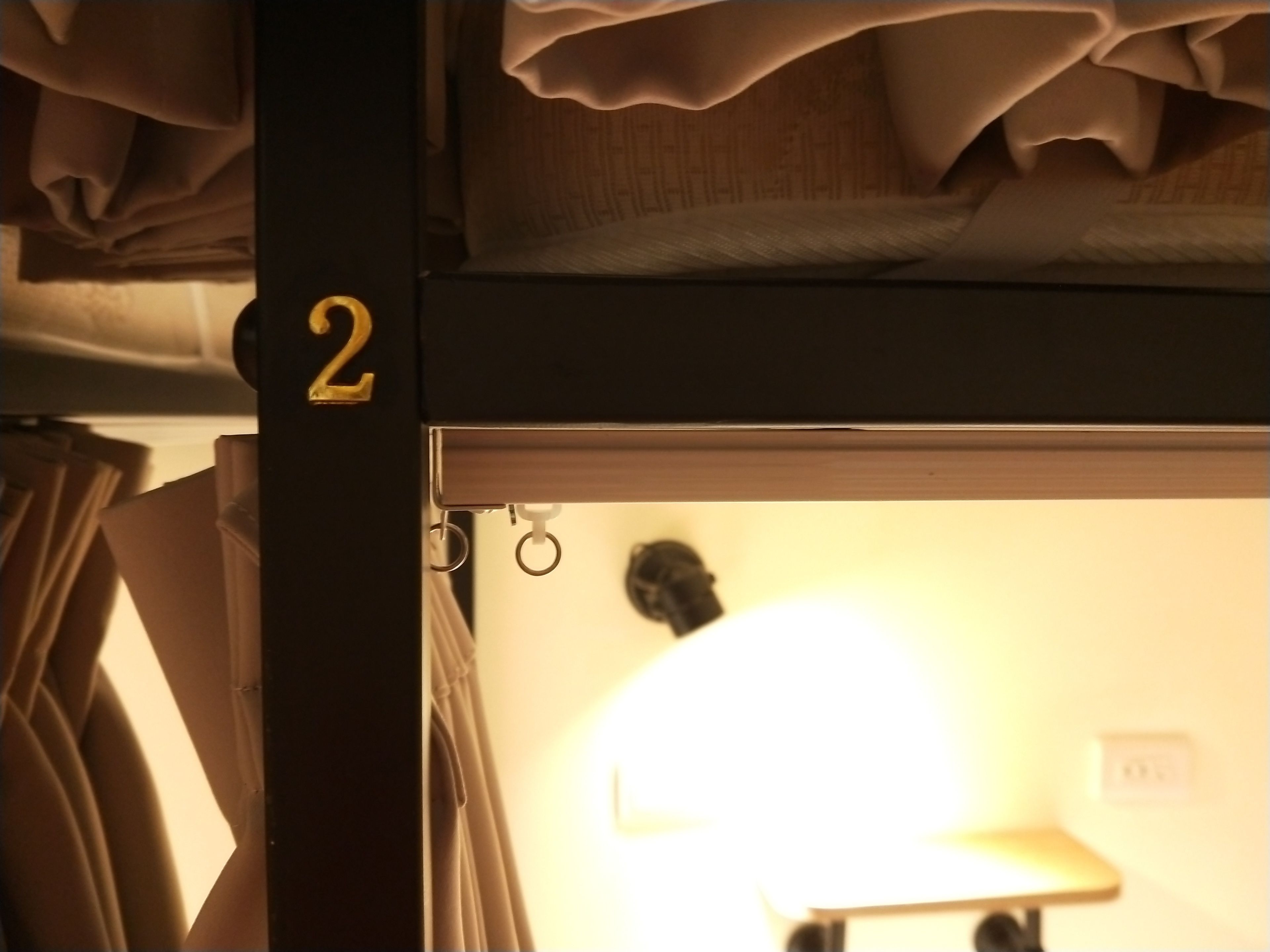 A bunk bed with a visible number '2' on the side, a curtain, and a partially visible room interior with a lamp.