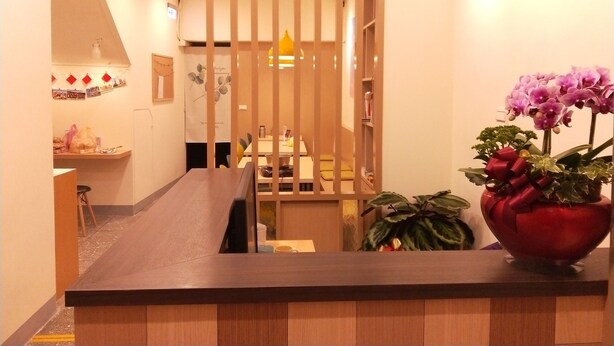 A hotel reception area with a wooden counter, a clock on the wall, and a potted orchid on the counter. - Fu Ao Wo & Hostel (Nangan)