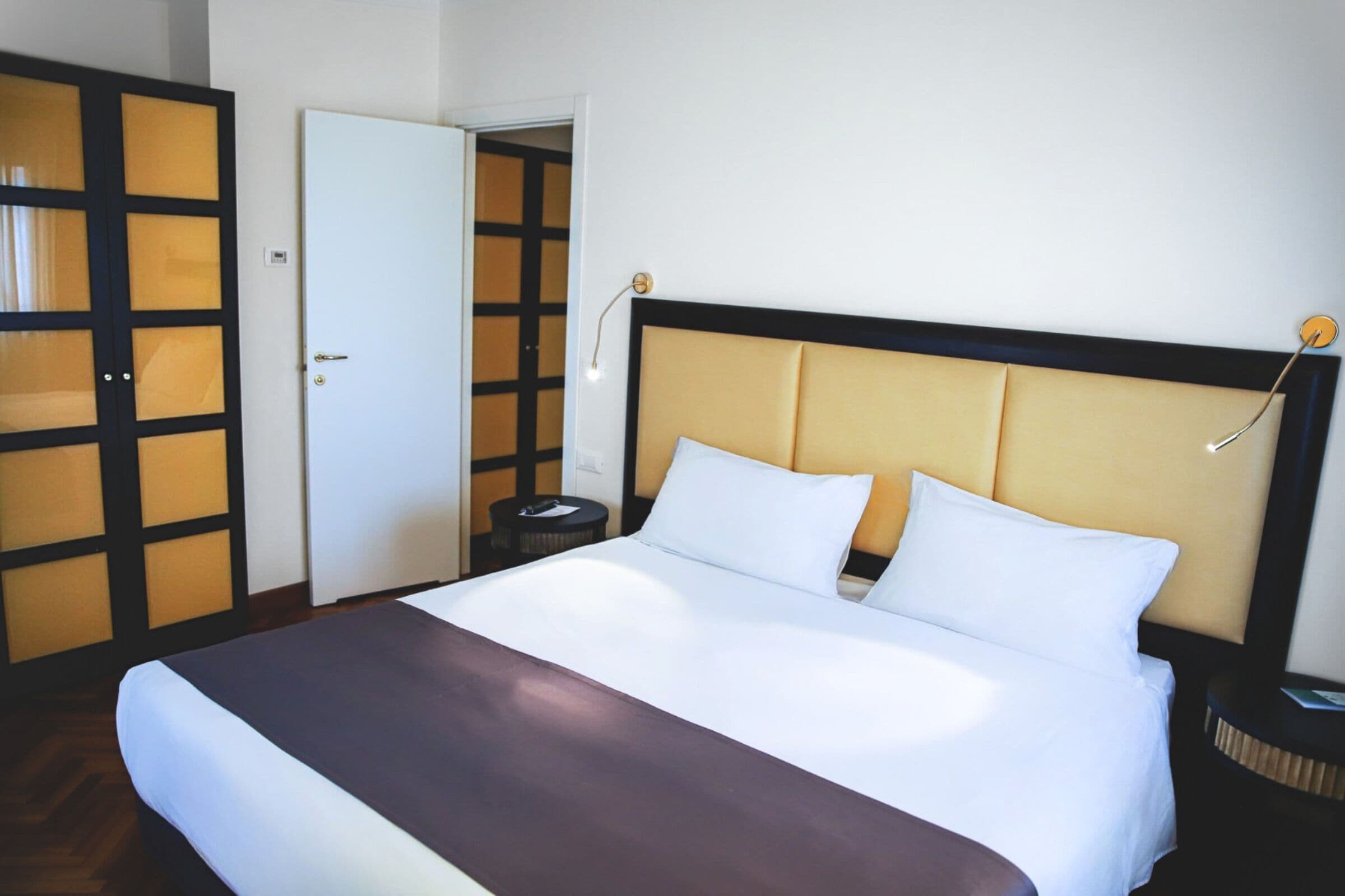 Une chambre d’hôtel comprenant un lit, une table de chevet, une commode, une armoire et une porte.