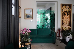 A green sofa, a vase of flowers, and a painting on the wall. - Torrione Hotel (Reggio Calabria)