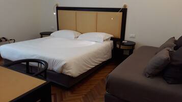 A hotel room with a bed, a small table, a sofa, and a nightstand with a lamp.