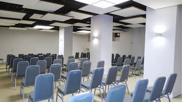 Una sala conferenze con file di sedie, un moderno design del soffitto e pareti bianche.