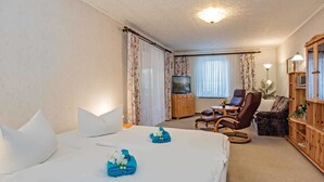 A hotel room with a bed, a TV, a seating area with a chair and a table, and a wooden cabinet. - Haus Ückeritz Bauernsuite - Haus Ückeritz Bauernsuite (Ückeritz)