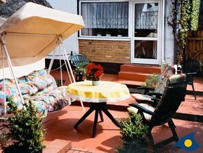 Un patio con una mesa redonda, sillas, un sillón colgante y una pequeña planta en maceta.