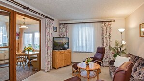 A living room with a television, a sofa, a dining table with chairs, and a window with curtains. - Haus Ückeritz Bauernsuite - Haus Ückeritz Bauernsuite (Ückeritz)