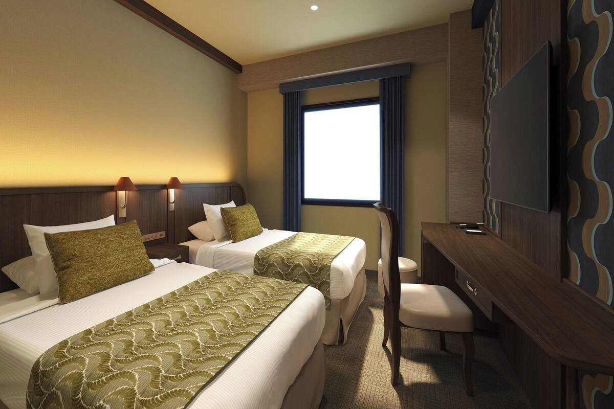 A hotel room with two beds, a desk, a chair, a TV, and a window with curtains.