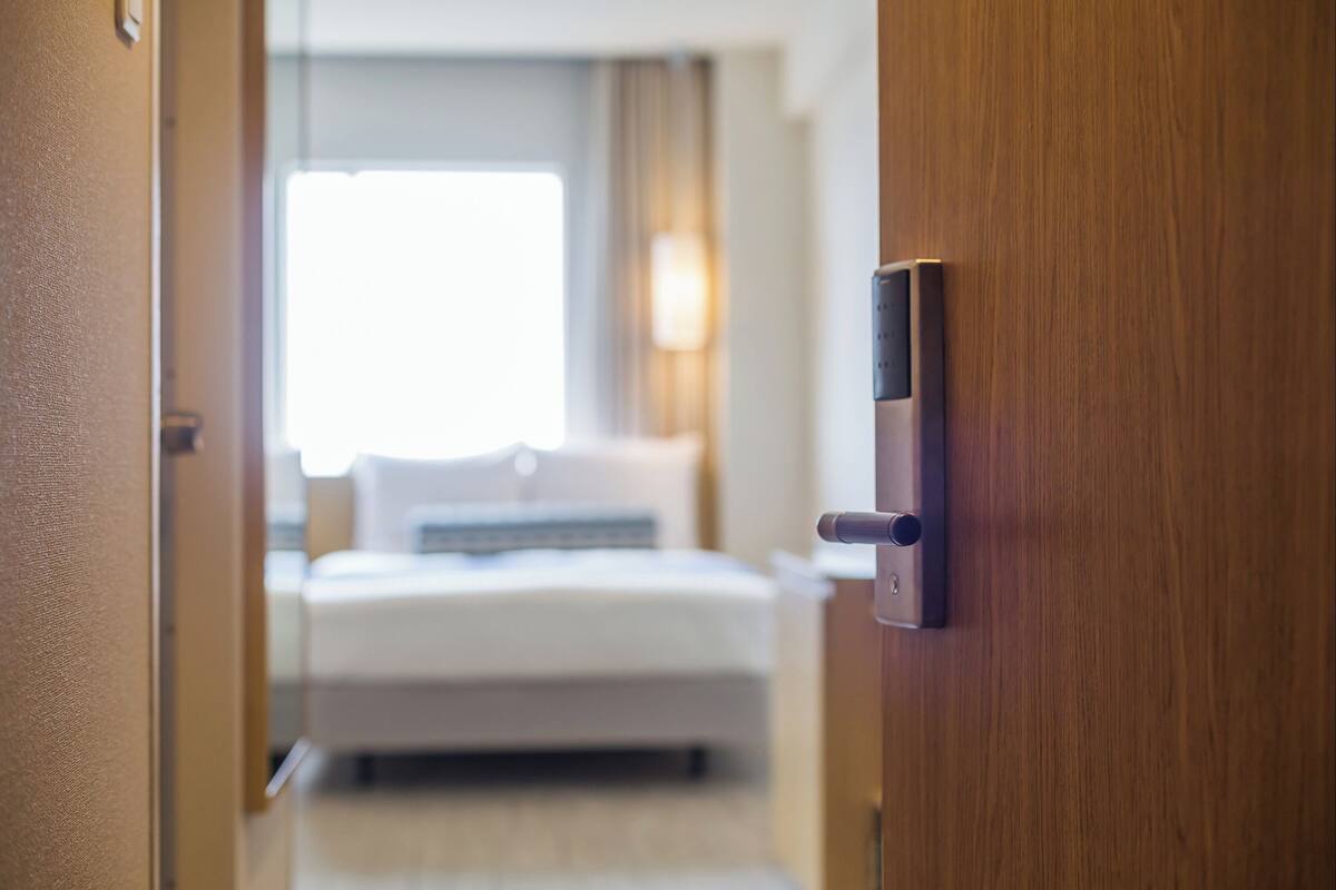 A hotel room with a bed, a bedside table, and a door with a lock.