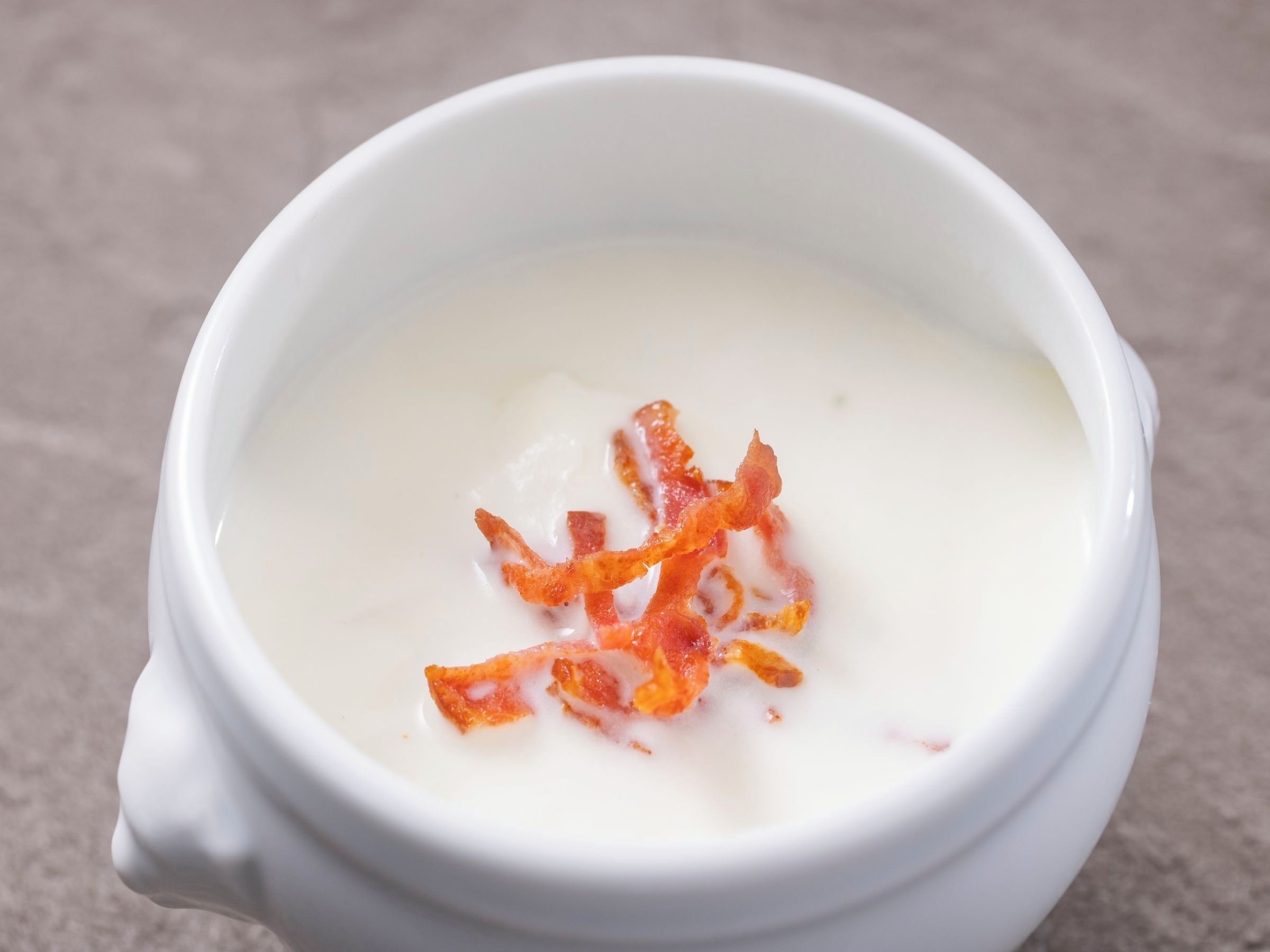 A white ceramic bowl with a creamy substance and crispy bacon bits on top.