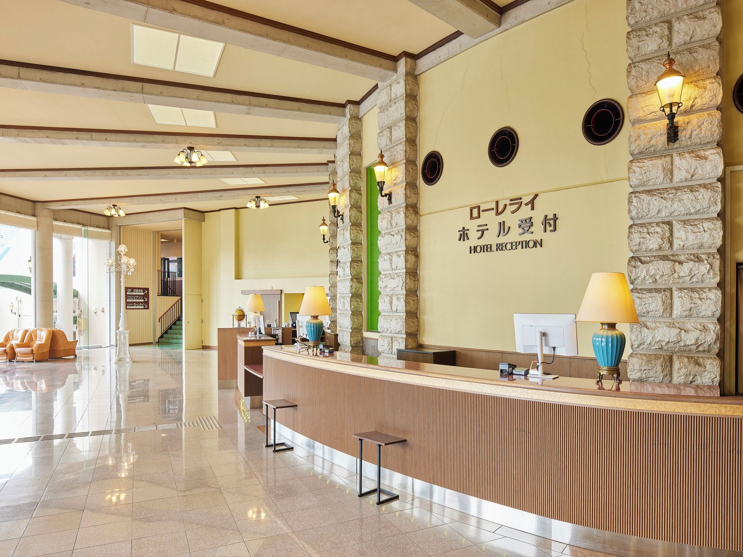 A hotel reception area with a stone wall, reception desk, and two lamps.