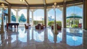 A spacious lobby with large windows, a grand piano, comfortable seating, and a polished floor. - Hotel Lorelei (Sasebo)