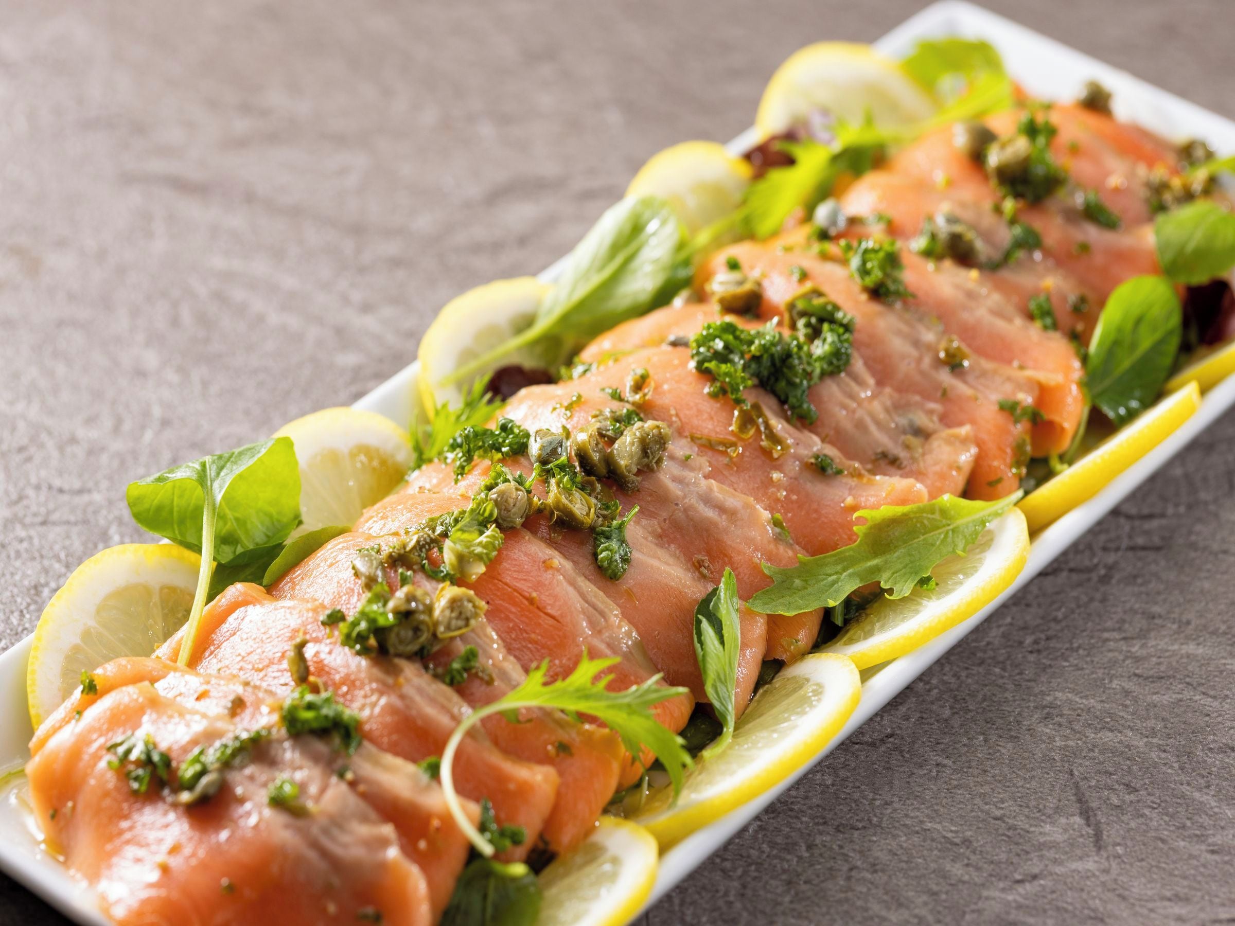 A plate of smoked salmon garnished with herbs and lemon slices.