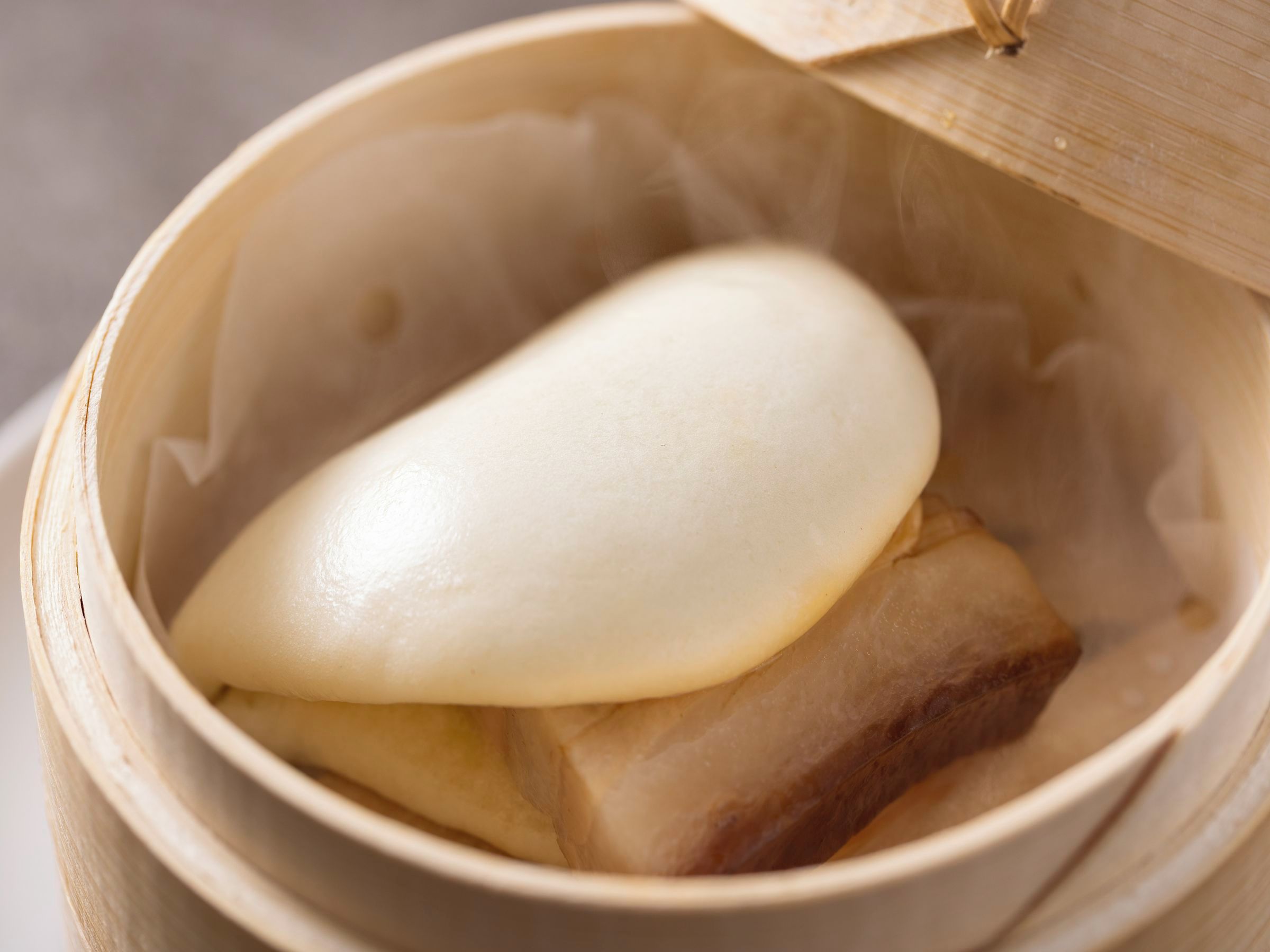 A bamboo steamer with a lid, containing a white food item and a brown item.
