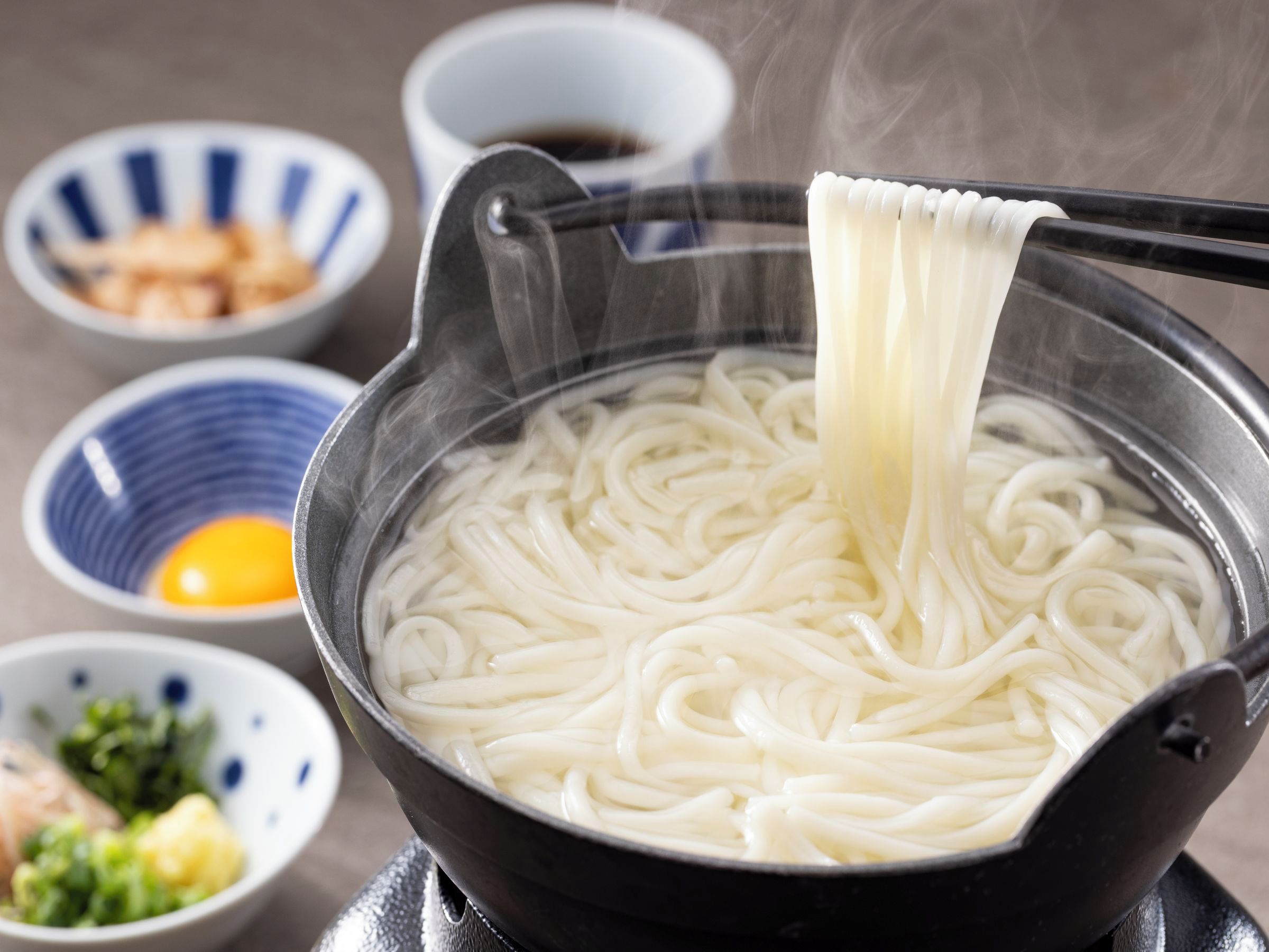 A bowl of ramen noodles being lifted from a pot.