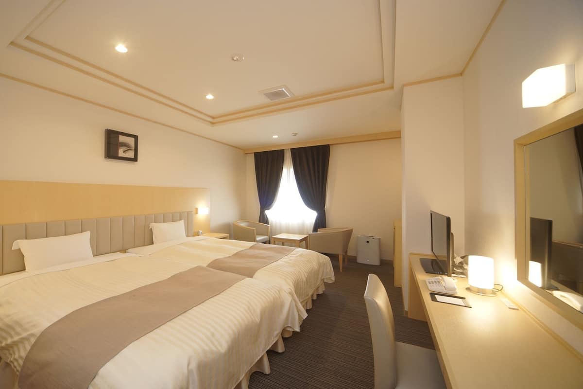 A hotel room with a large bed, a desk, a chair, a television, and a mirror.